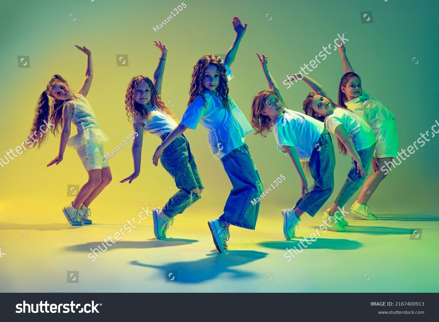 Happy children dancing. Group of children, little girls in sportive casual style clothes dancing in choreography class isolated on green background in yellow neon light. Concept of music, fashion, art Stock-foto